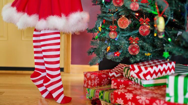 Child in striped socks standing in front of Chirstmas tree and presents.