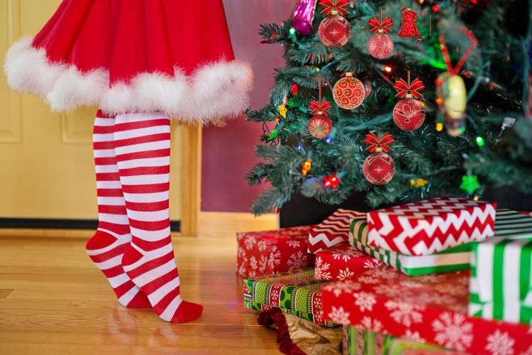 Child in striped socks standing in front of Chirstmas tree and presents.